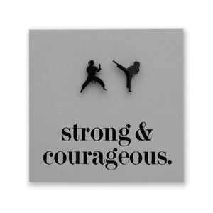 A square gray wall art print featuring two black silhouettes of martial artists in action above the phrase 'strong & courageous.' in black serif text, shown against a white background.