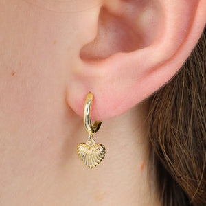 Gold hoop earring with a shell charm worn by a person