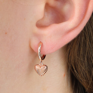 Rose gold heart earrings shown in a girls ear.