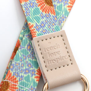Floral-patterned strap with a beige tag featuring 'teach love inspire' on a white background