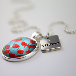Necklace with a pendant featuring red flowers on a blue background and a tag that says 'STRONG'.