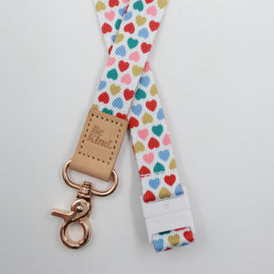 Be Kind embossed on a white lanyard with multicoloured hearts and tan trim and a lobster clasp.