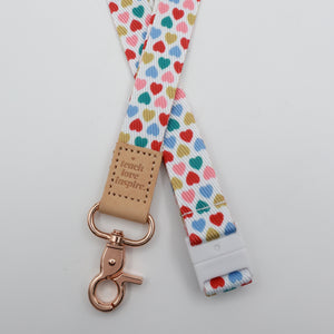 Teach Love Inspire embossed on a white lanyard with multicoloured hearts and tan trim and a lobster clasp.