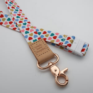 Teach Love Inspire embossed on a white lanyard with multicoloured hearts and tan trim and a lobster clasp.