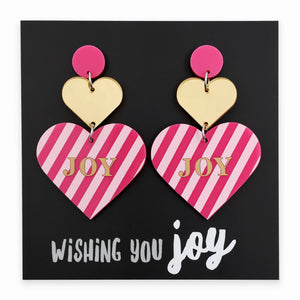 Heart-shaped earrings with pink and gold design on a black card with 'Wishing You Joy' text.