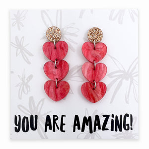 Red heart-shaped earrings on a card with 'YOU ARE AMAZING!' text