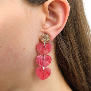Close-up of an ear wearing a pink heart-shaped earring with a gold accent.