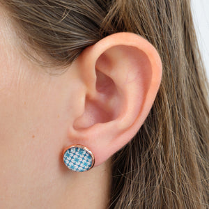 Close-up of an ear wearing a blue patterned earring with a white background