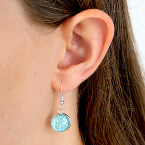 Close-up of an ear wearing a turquoise earring with a white background