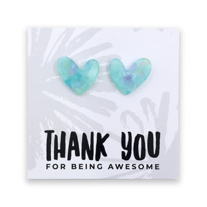 A pair of heart-shaped stud earrings in a translucent light blue and mint green resin with subtle purple swirls, displayed on a white card that reads 'THANK YOU FOR BEING AWESOME'.