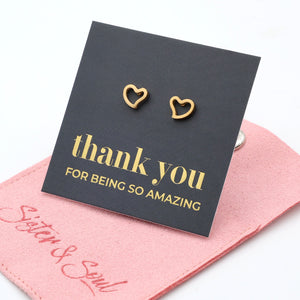 Gold heart-shaped earrings on a 'thank you' card with pink pouch underneath