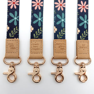 Four floral lanyards with motivational phrases and gold hooks on a white background