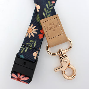 Floral-patterned lanyard with a gold clasp and 'so loved' tag on a white background