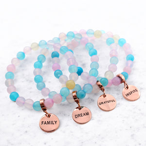 Set of colorful beaded bracelets with rose gold charms on a light background