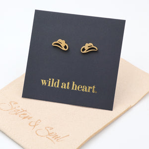 Gold cowgirl hat earrings on a black card with 'wild at heart.' text, placed on a oat pouch with 'Sister & Soul' branding.