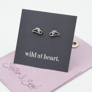 Silver cowgirl hat earrings on a black card with 'wild at heart.' text, placed on a mauve pouch with 'Sister & Soul' branding.