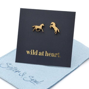 Gold horse earrings on a black card with 'wild at heart.' text on a blue pouch