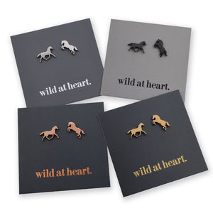 Four pairs of horse stud earrings displayed on dark gray backing cards with the phrase "wild at heart." printed on them.