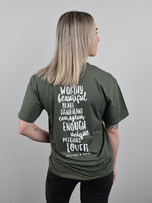 A woman with blonde-highlighted hair is shown from the back wearing an olive green t-shirt with white hand-lettered text on the back. The text reads 'WORTHY beautiful BRAVE SIGNIFICANT courage ENOUGH unique precious LOVE' and 'BAYTEEN & BOYL'.