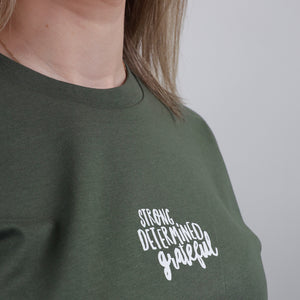 Close-up of a person wearing an olive green crewneck sweatshirt with the words 'STRONG. DETERMINED.