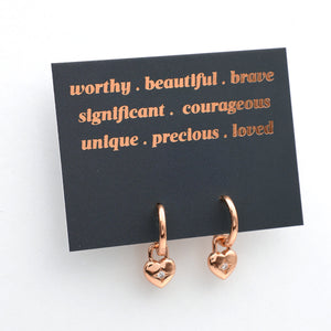 Rose gold heart-shaped earrings on a card with positive affirmations