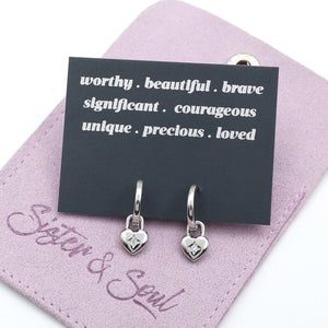 Silver heart-shaped earrings on a pink card with motivational text and 'Sister & Soul' branding.