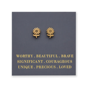Gold flower-shaped earrings on a dark gray card with motivational text.
