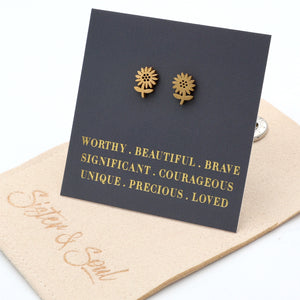 Gold sunflower earrings on a card with motivational phrases, displayed on a beige cloth.