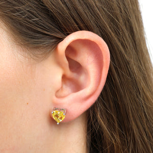 Close-up of an ear wearing a yellow heart-shaped earring with brown hair.