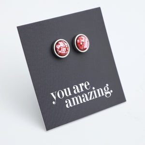 Red glittery stud earrings on a black card with 'you are amazing' text