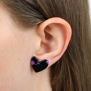 A close-up of a person's ear wearing a glossy heart-shaped stud earring in black with purple swirl accents.