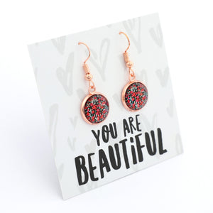 Earrings with glittery pink and red stones on a card with 'You are Beautiful' text.
