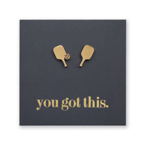 A pair of gold-tone pickleball-themed stud earrings mounted on a dark charcoal square backing card with the phrase 'you got this.' in gold lettering, shown against a plain white background.