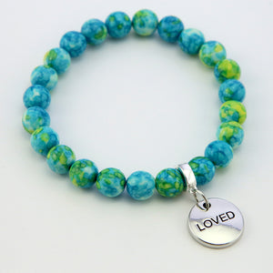 Stone bracelets with blue and green stone beads and silver charms with the words 'strength', 'loved', and 'inspire' on them.