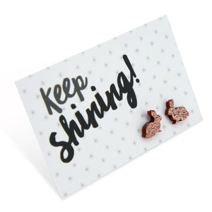 A pair of rose gold glitter acrylic bunny stud earrings on a white background with the text 'Keep Shining!' written in black.