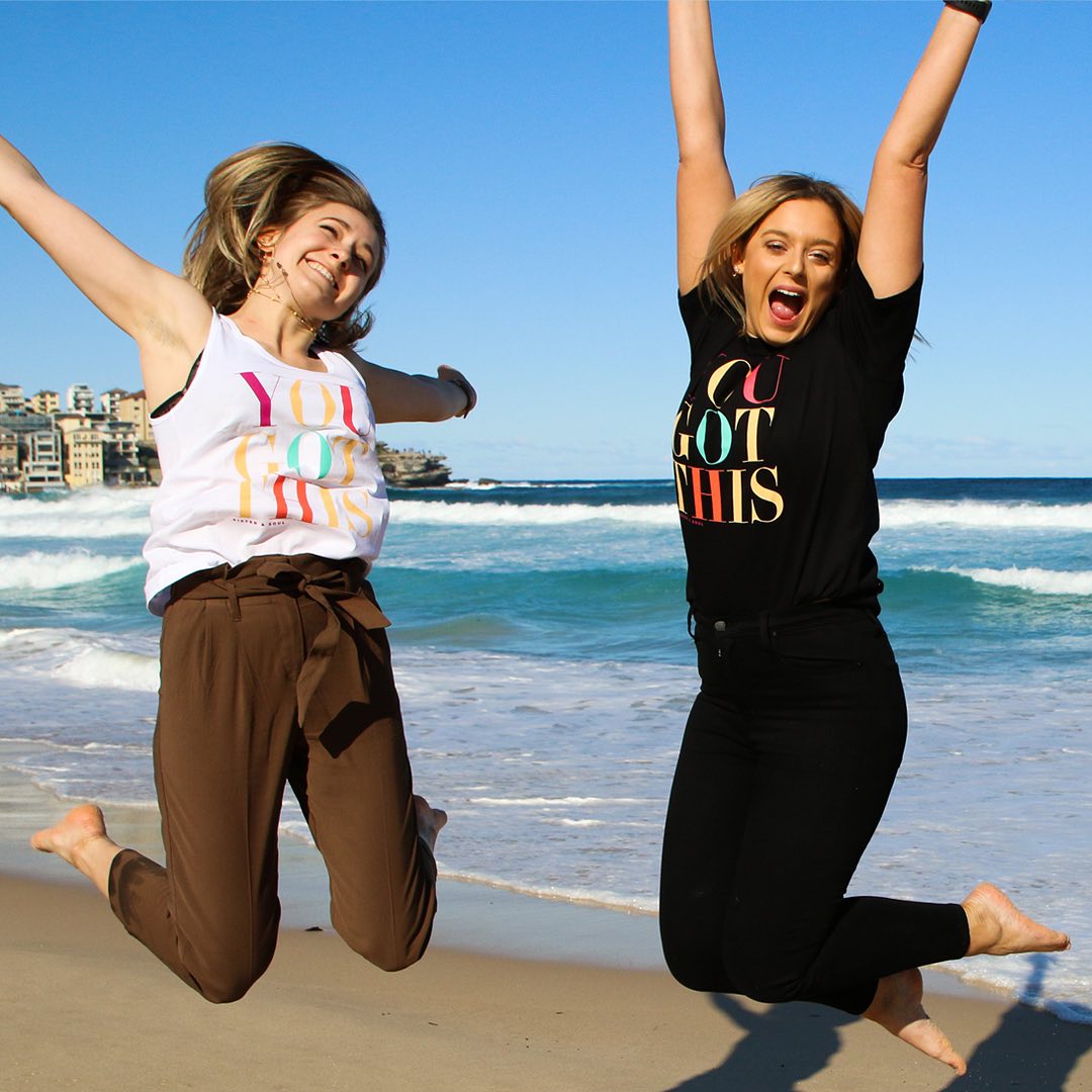 Two women at beach celebrating their Self-Worth and wearing t-shirts with positive message
