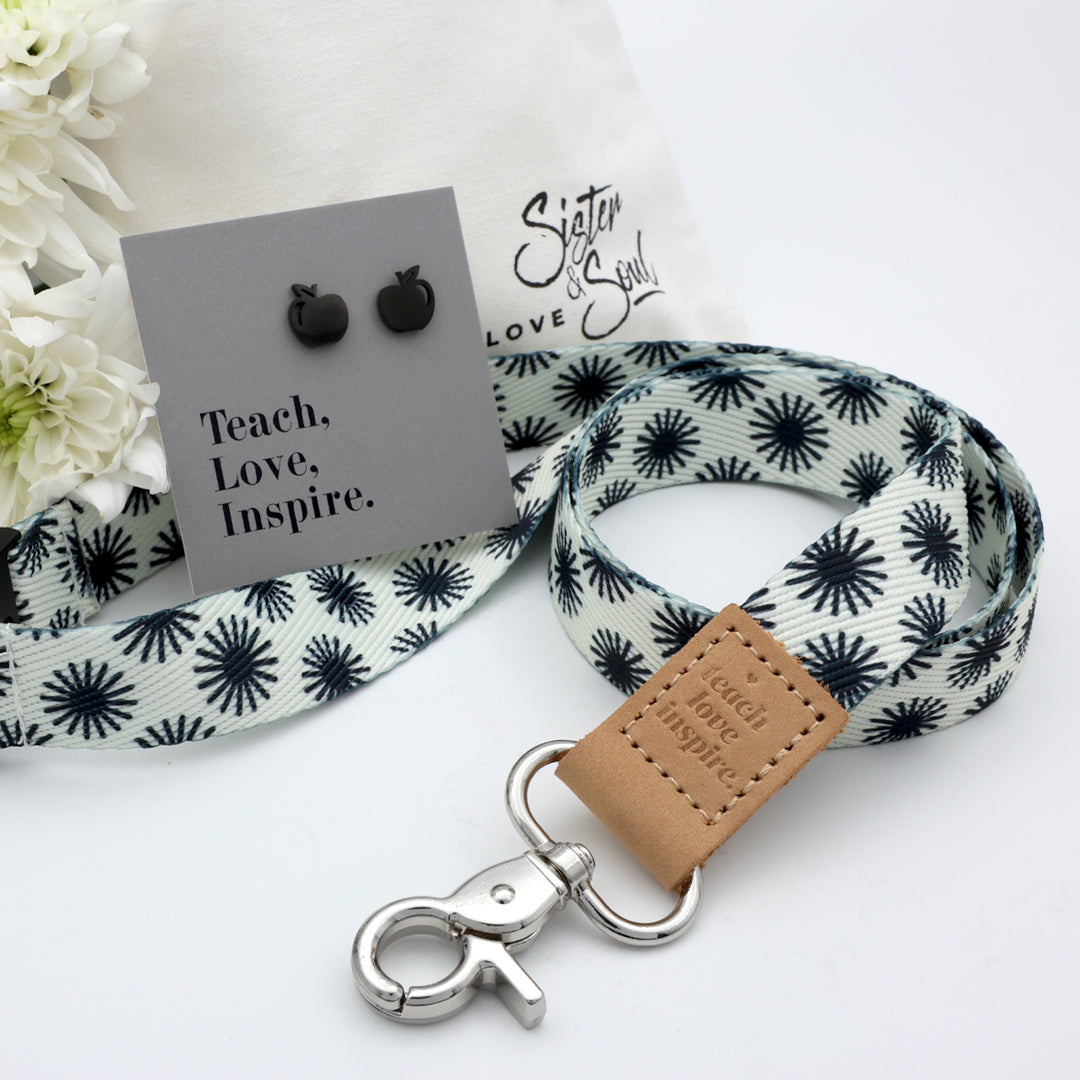 Product set with white flowers, drawstring bag, black and white patterned lanyard, and earrings on a white background.