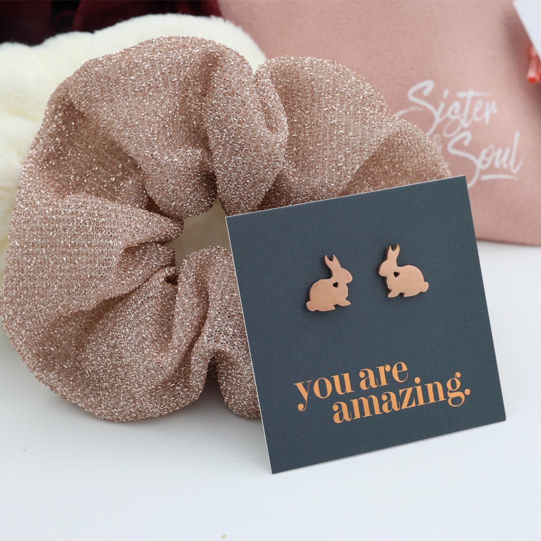 Rose gold scrunchie and bunny earrings on a card with 'you are amazing' text.