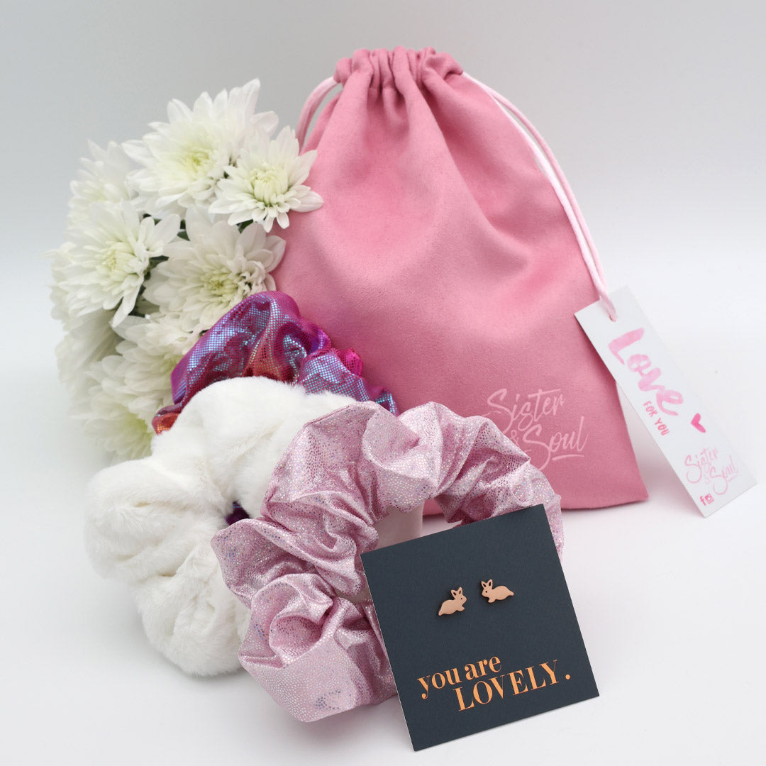 Pink drawstring bag with flowers, scrunchies, and earrings on a light gray background