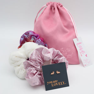 Pink drawstring bag with scrunchies and earrings on a white background