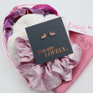 Earring box with 'you are LOVELY' text and bunny earrings on a pink textured background