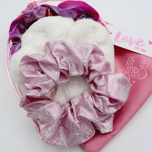Pink glitter scrunchie on a white heart-shaped pillow with a pink heart-shaped pouch in the background.