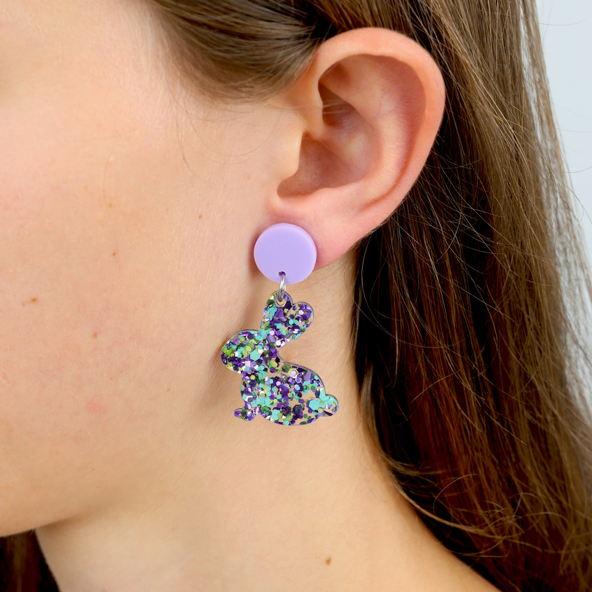 A pair of colorful acrylic bunny-shaped earrings on a girls ear