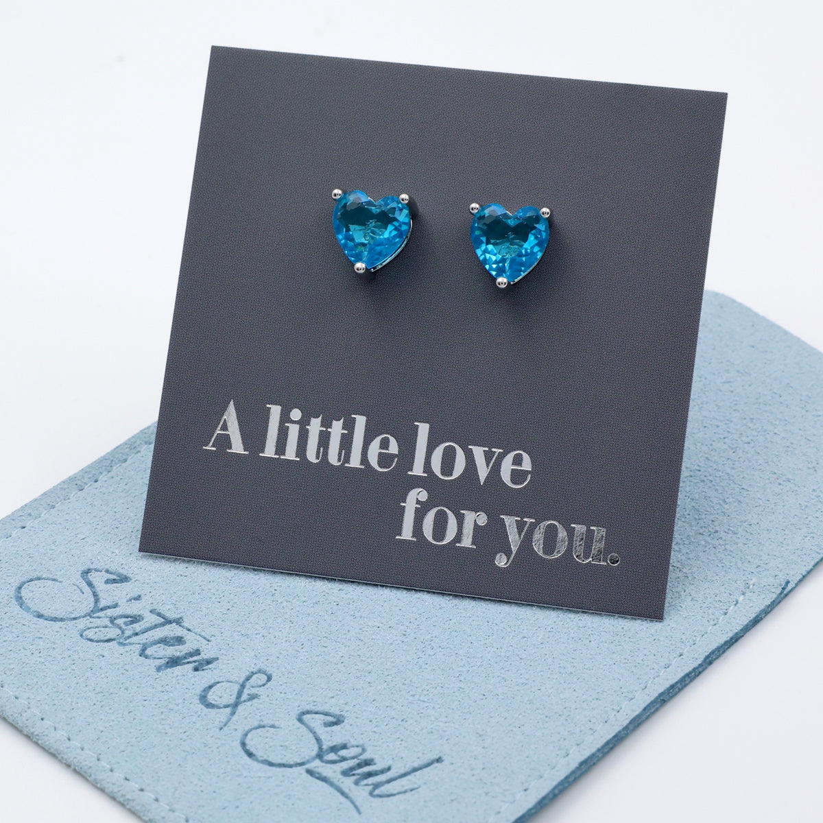 Heart-shaped blue gemstone earrings on a 'A little love for you' card with 'Sister & Soul' branding.