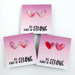 Heart-shaped earrings on a card with 'all kinds of strong' text