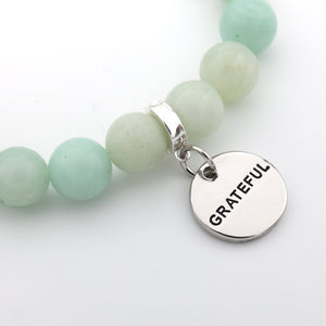 Mint green beaded bracelet with a 'GRATEFUL' charm on a white background