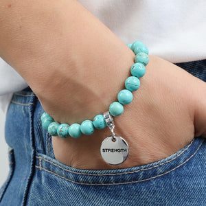 Turquoise beaded bracelet with a 'STRENGTH' charm on a wrist, wearing jeans.