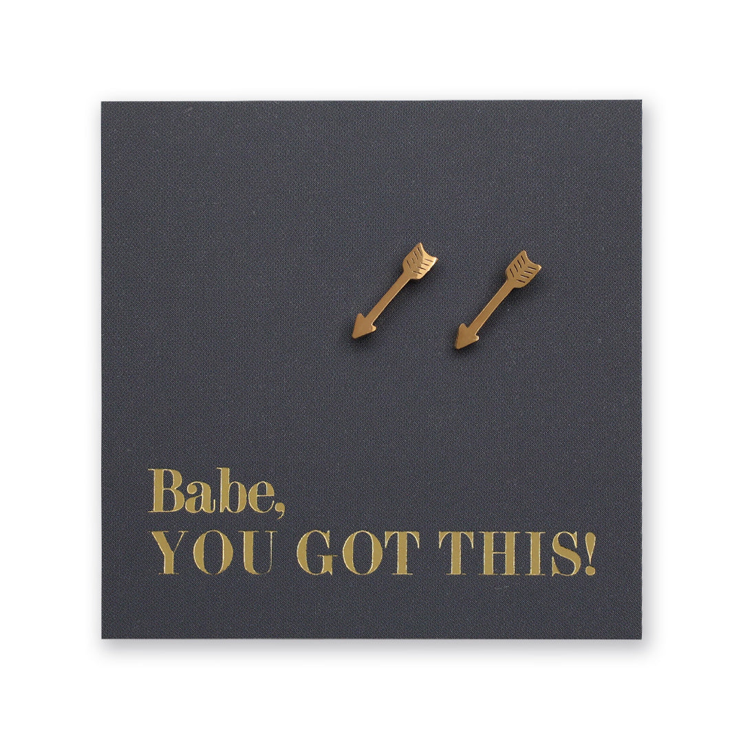 A pair of small gold arrow-shaped stud earrings displayed on a dark charcoal square backing card with the phrase 'Babe, YOU GOT THIS!' in gold lettering, shown against a plain white background.