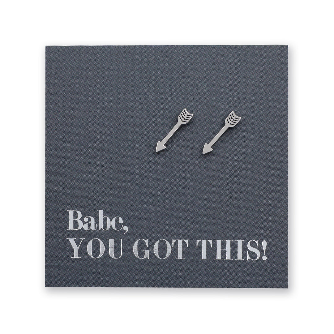 Two silver arrow-shaped stud earrings displayed on a dark gray square backing card with the text 'Babe, YOU GOT THIS!' in silver lettering.