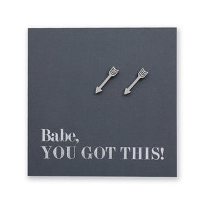 Two silver arrow-shaped stud earrings displayed on a dark gray square backing card with the text 'Babe, YOU GOT THIS!' in silver lettering.